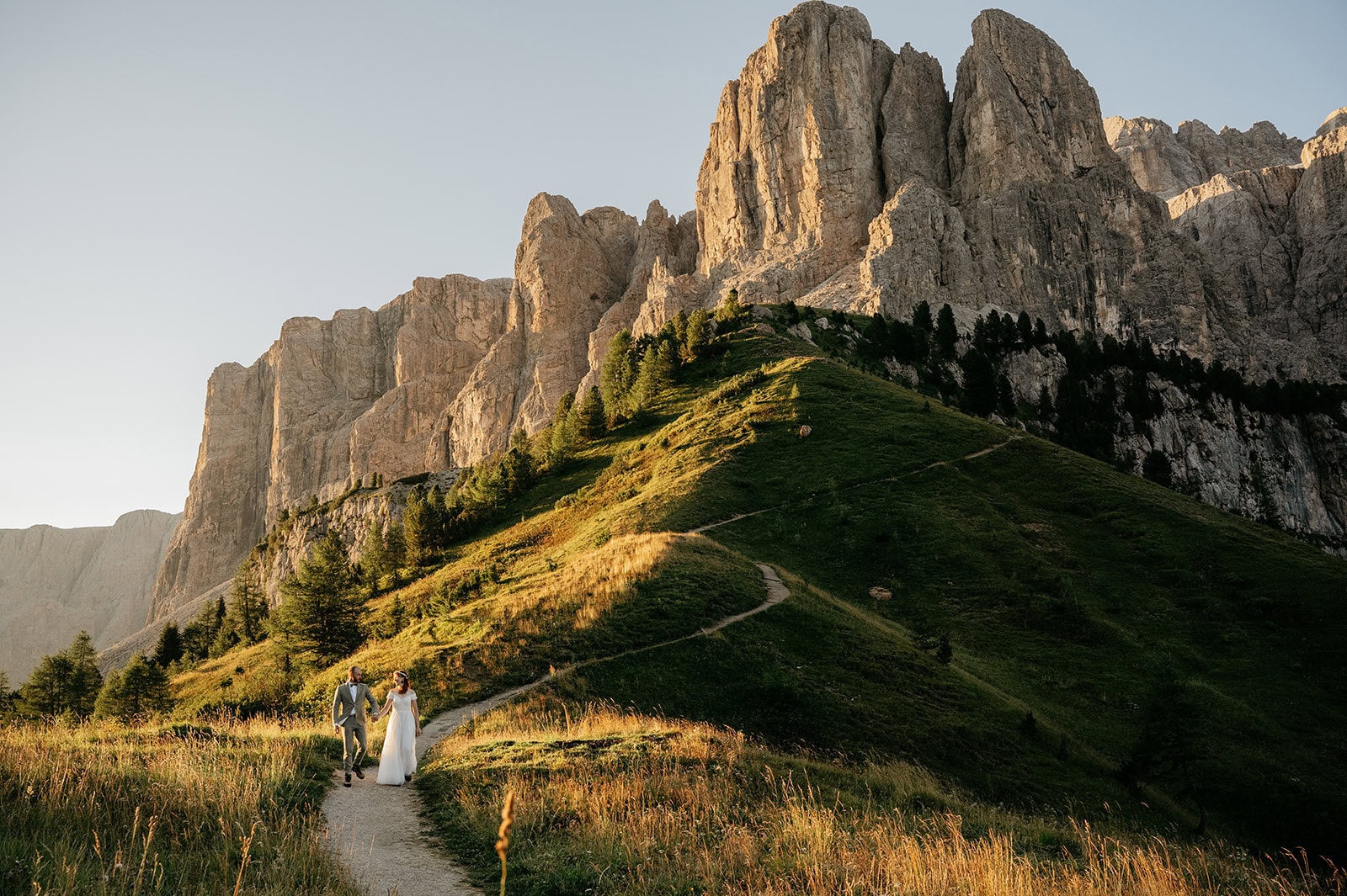 Couple walking on mountain path at sunset.