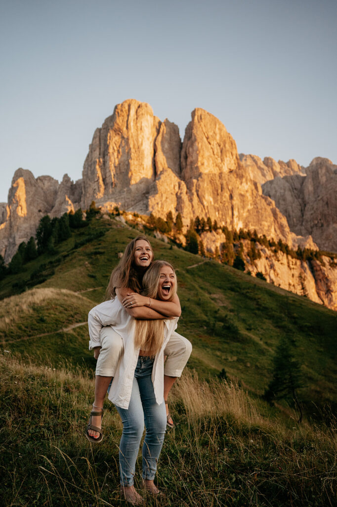 Two women enjoy a playful piggyback in mountains.