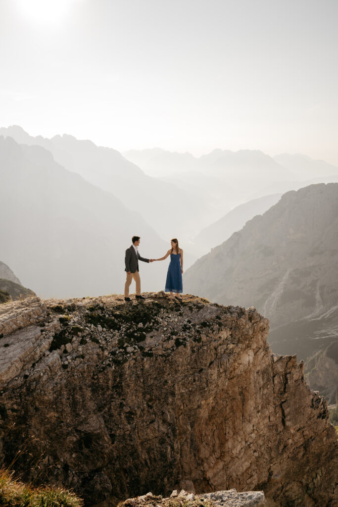 Couple holds hands on rocky mountain cliff