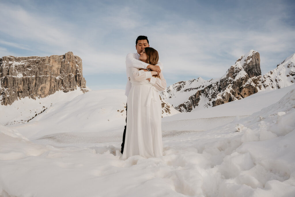 Couple embraces in snowy mountain landscape.