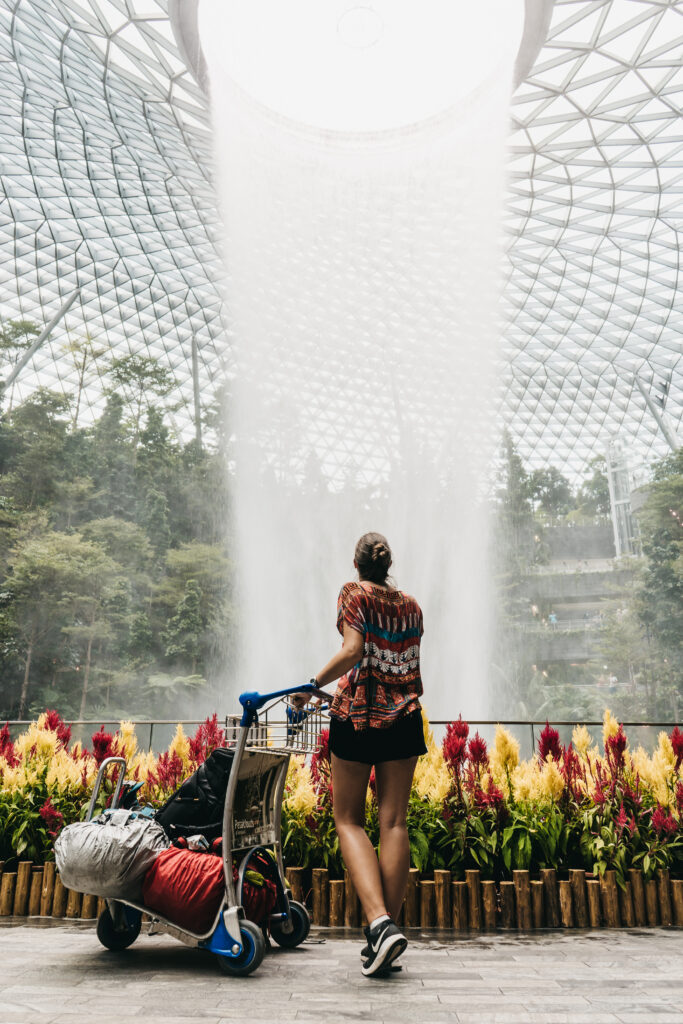 Naty Lizzy from the back with luggage cart looking at indoor waterfall in the Singapore Airport