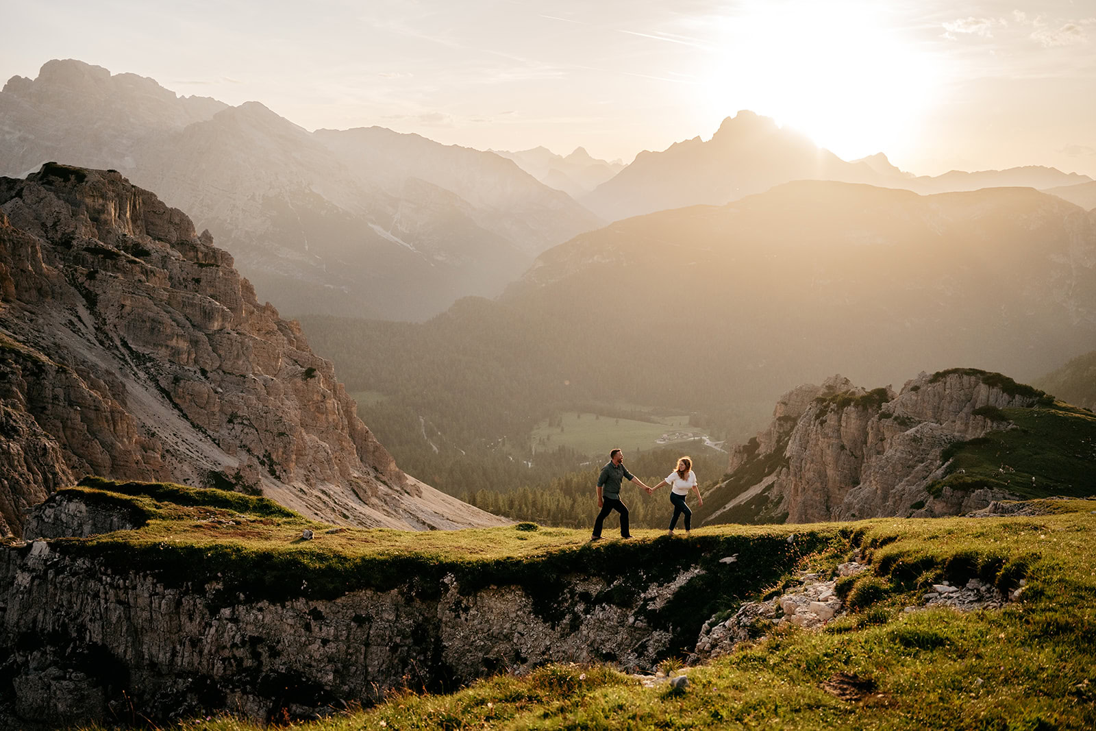 Couple holding hands on mountain at sunset.