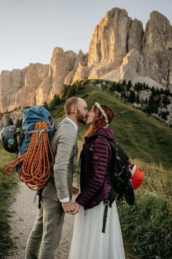 Couple kissing with climbing gear, mountain backdrop.