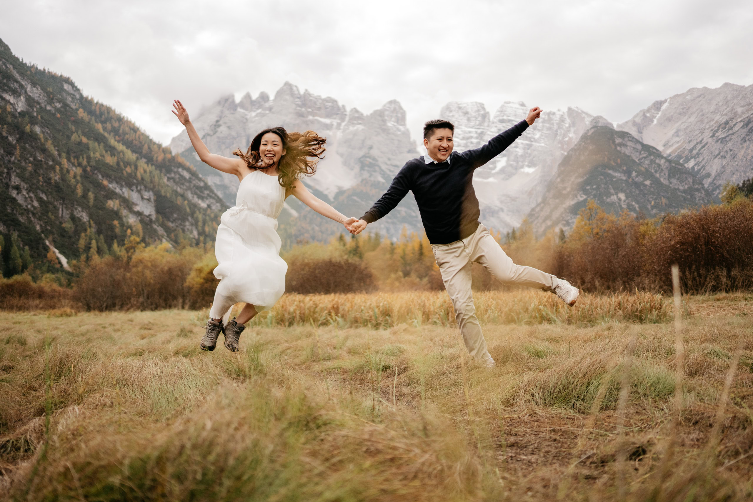 Couple joyfully jumping in a scenic mountain meadow.