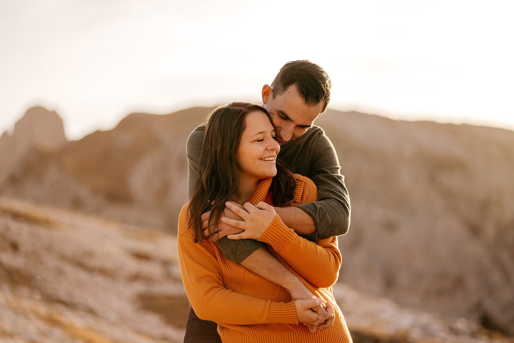 Couple embracing outdoors with mountain backdrop.