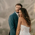 Couple embracing, mountain backdrop, wedding attire