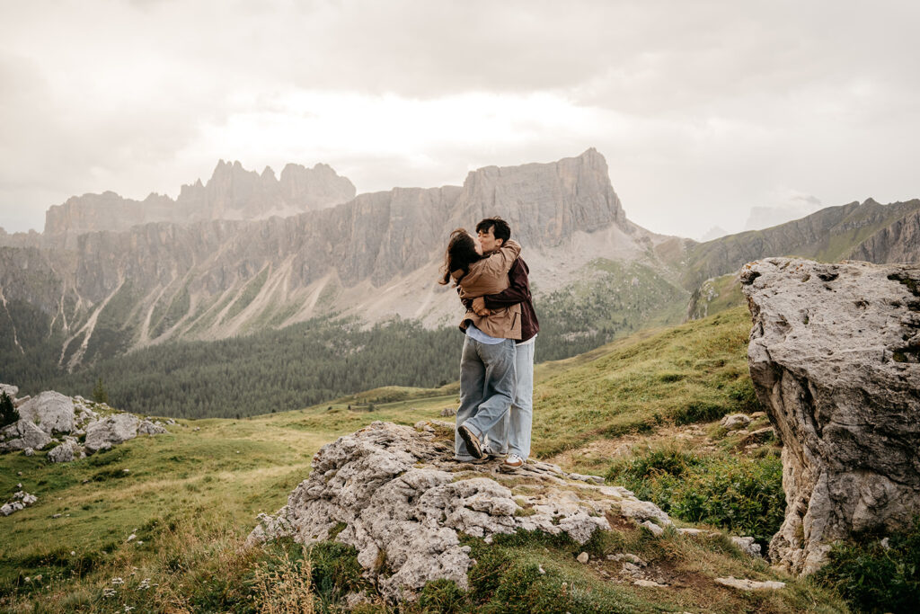 Couple embraces on mountain, scenic rocky background.