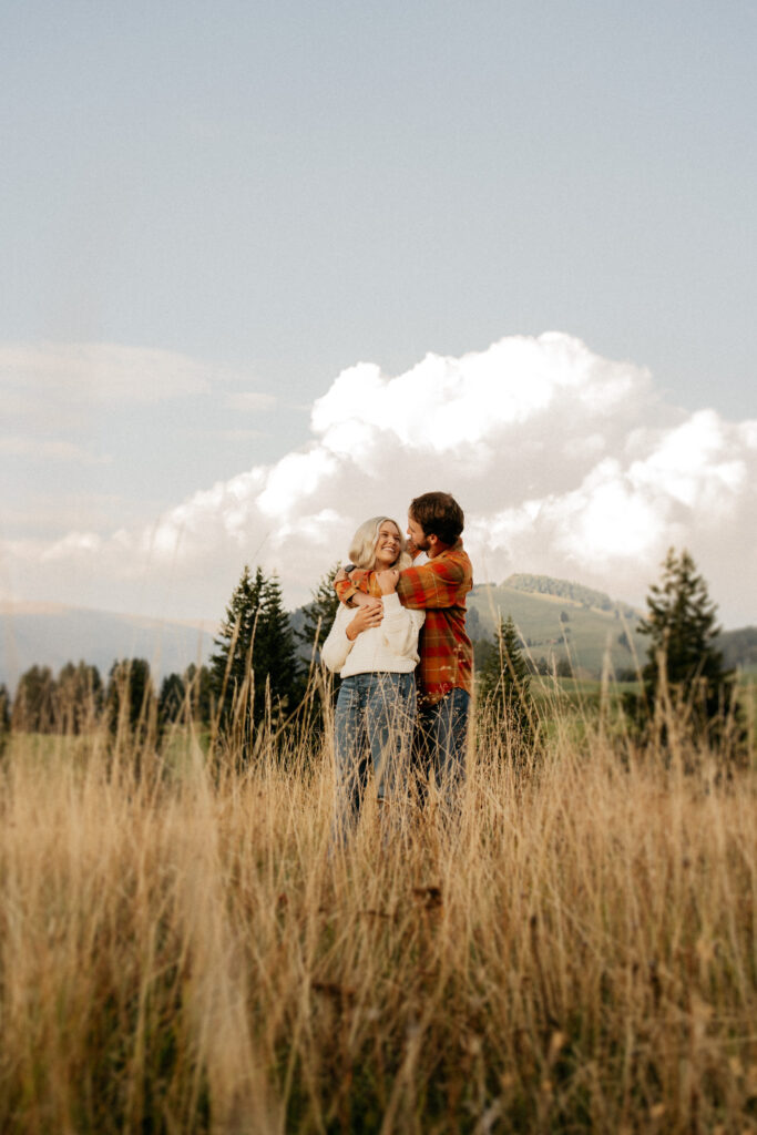 Couple embraces in scenic field with mountains.