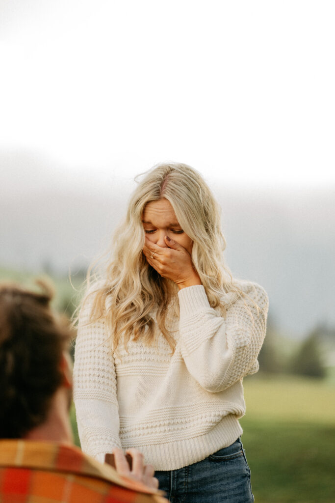 Surprised woman covering mouth during proposal outdoors.