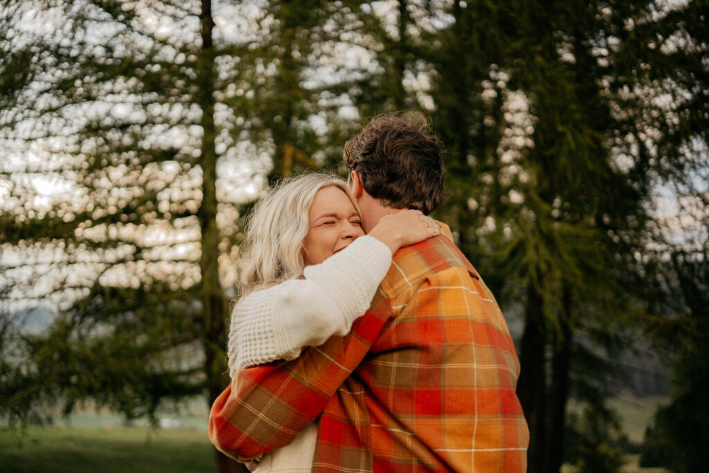 Couple hugging outdoors with trees in background.