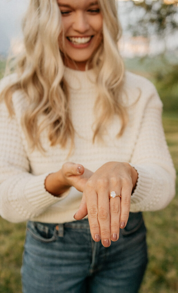 Smiling woman showing engagement ring outdoors.