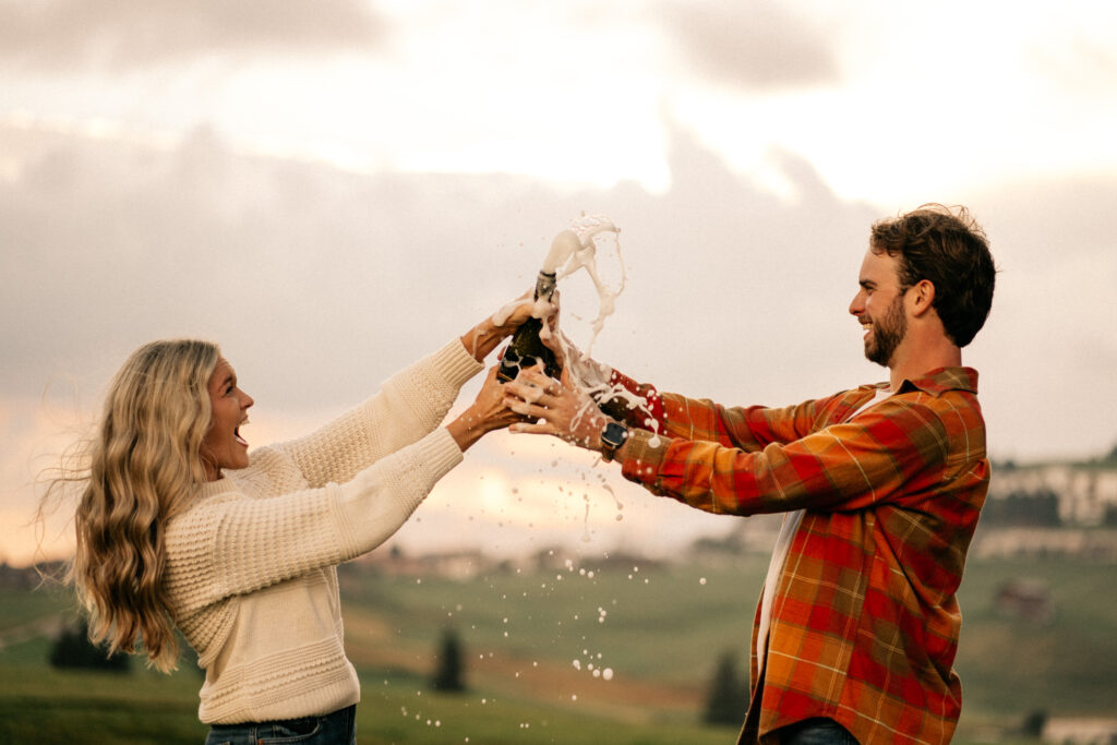 Couple celebrating with champagne outdoors at sunset.