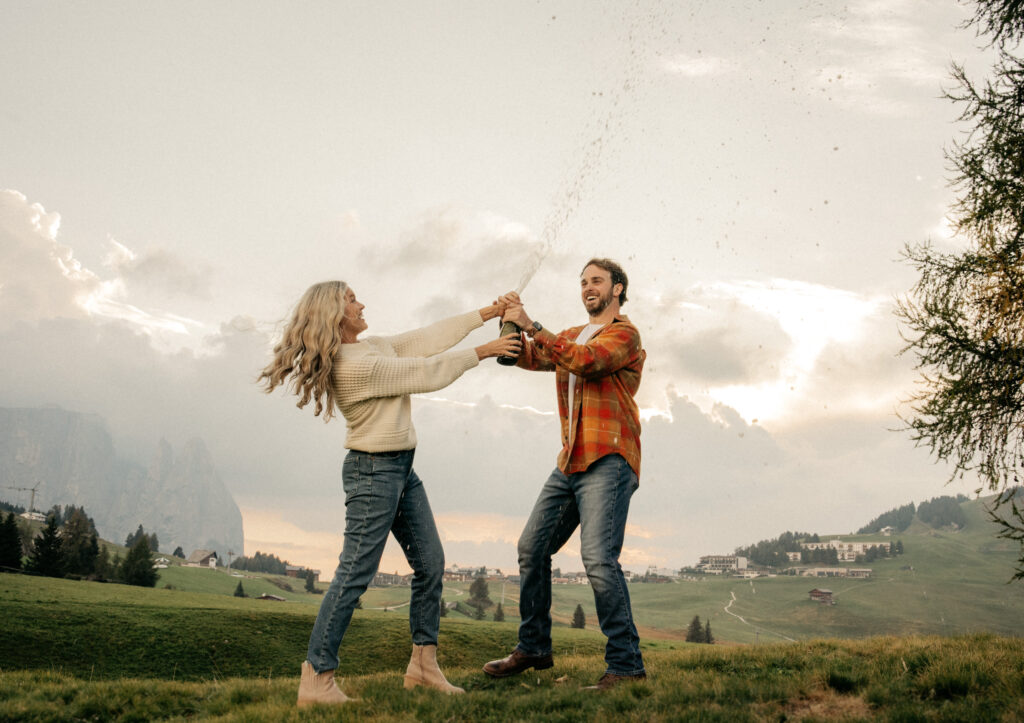 Couple celebrating with champagne in scenic field.