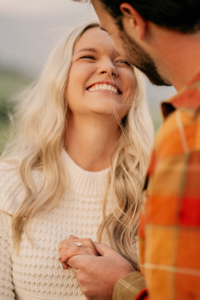 Smiling couple holding hands, engagement ring visible.