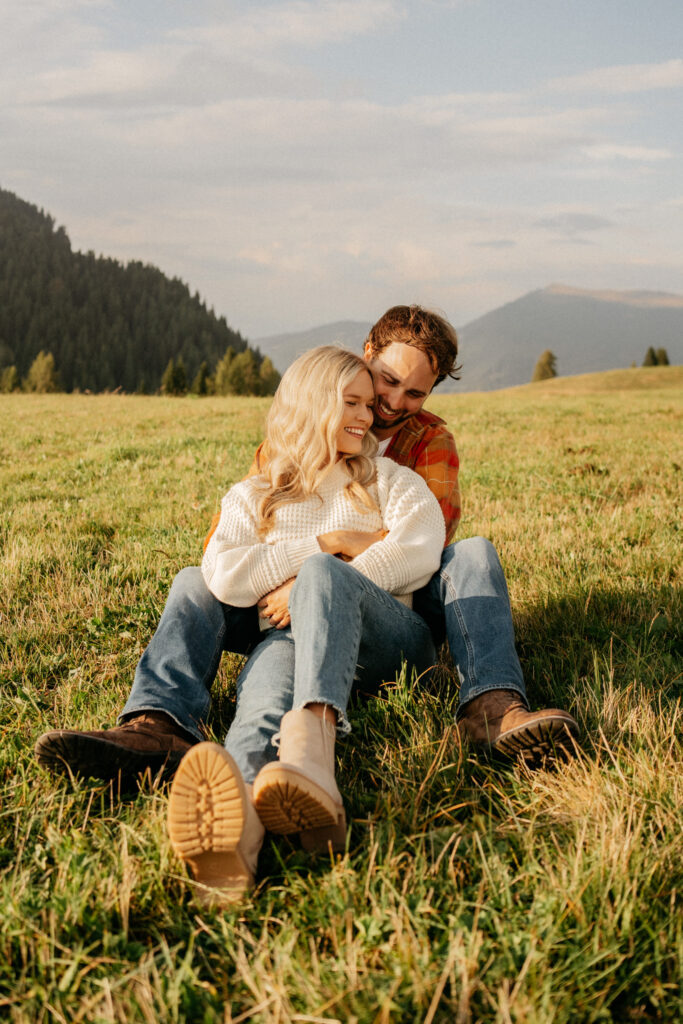 Couple sitting on grass with mountains behind.