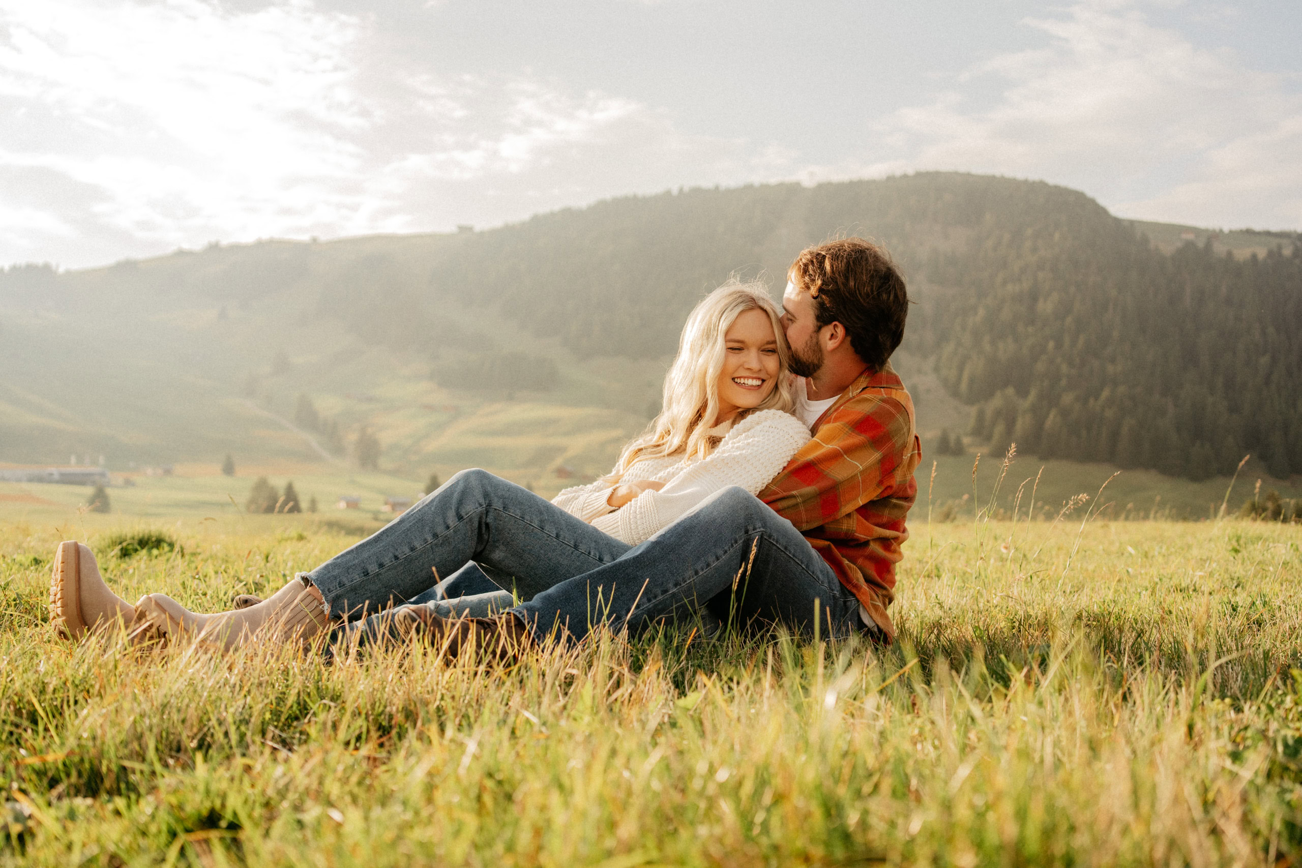 Couple smiling in sunny mountain meadow.