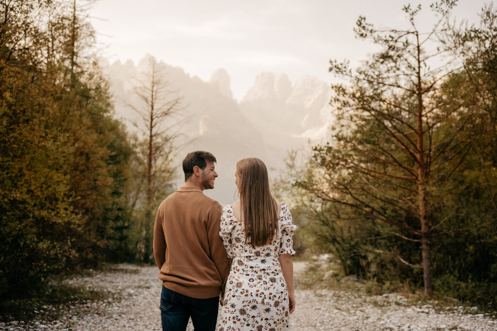 Couple walking on forest path toward mountains.