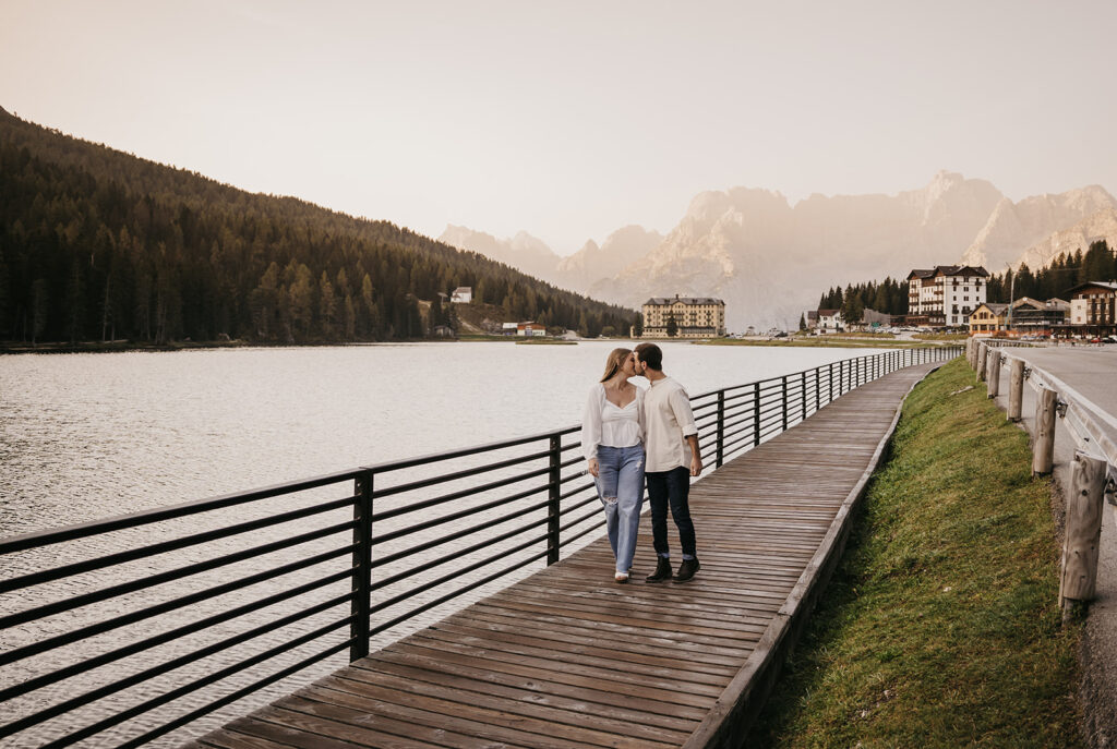 Couple walking on lakeside boardwalk at sunset.