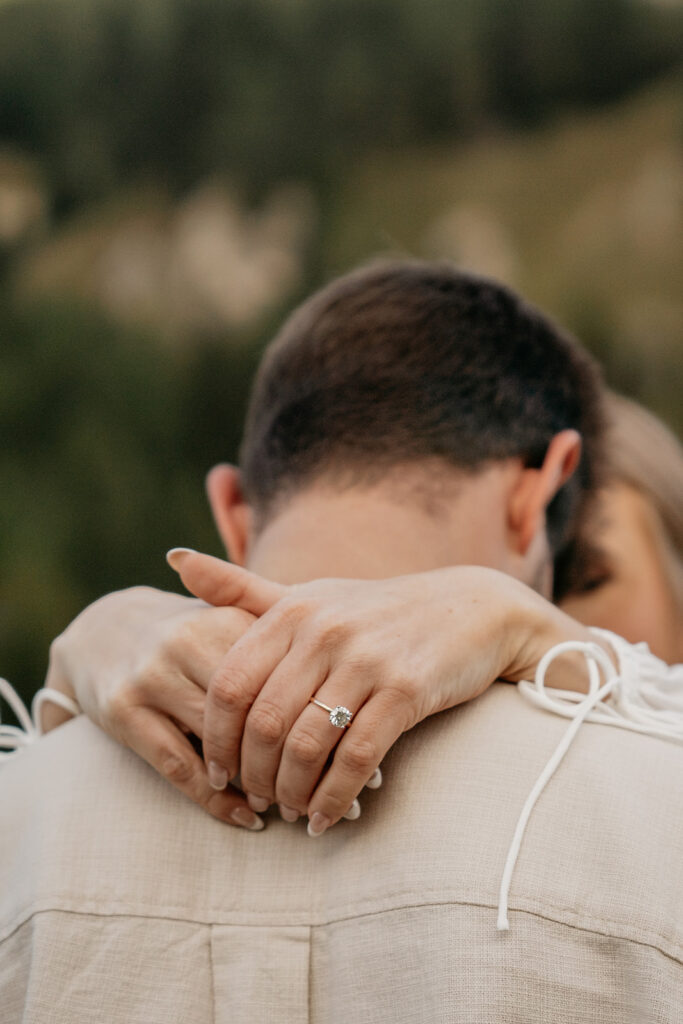 Close-up of couple hugging, engagement ring visible.