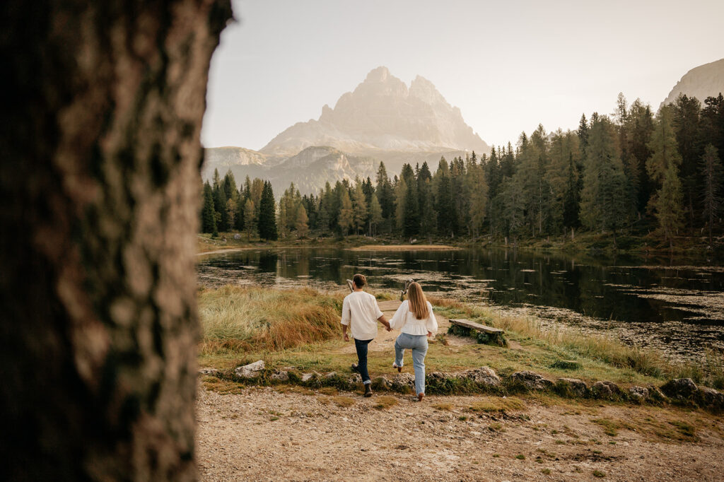 Couple walking by serene mountain lake in forest.