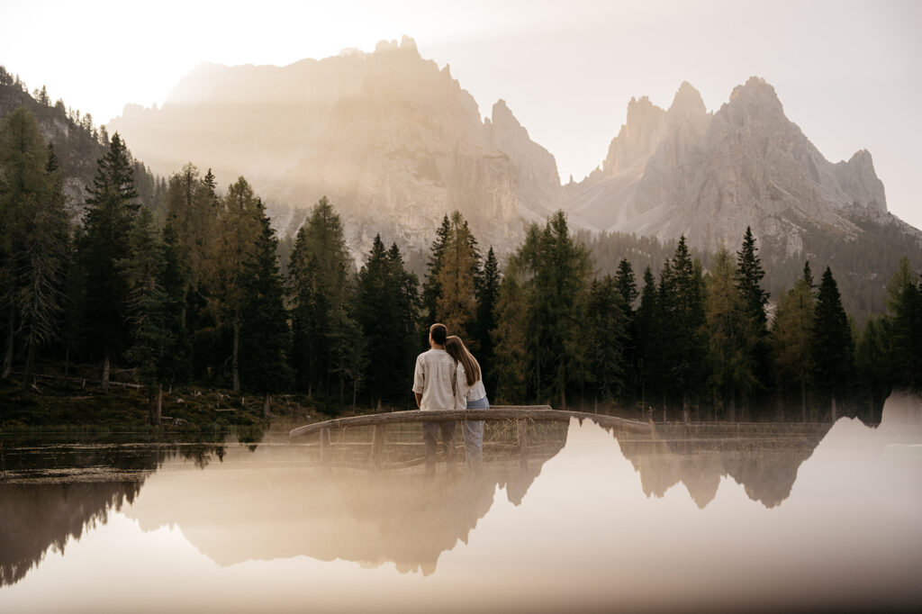 Couple embraces by mountain lake at sunrise.