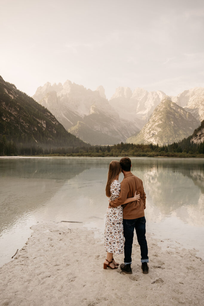 Couple embraces by mountain lake, serene landscape view.