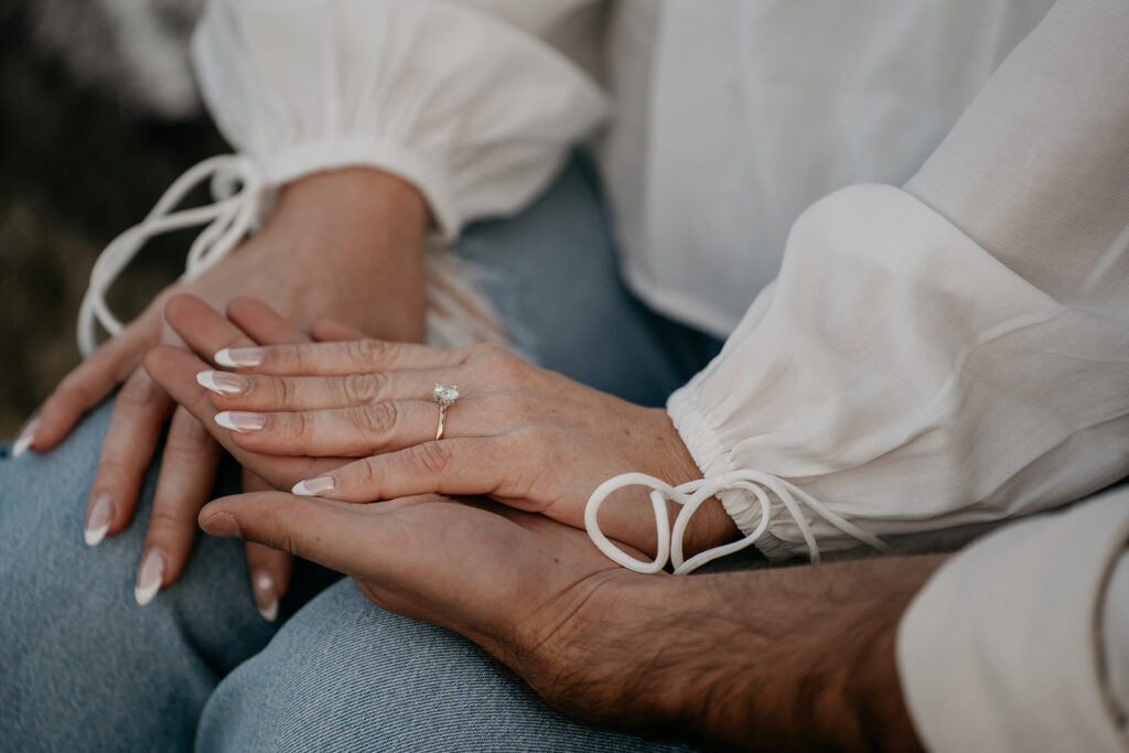 Engagement ring on woman's hand, hands intertwined.