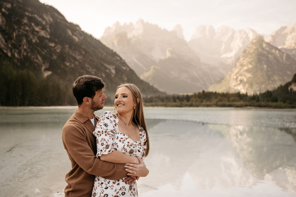 Couple embraces by mountain lake at sunset.