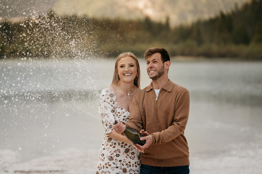 Couple celebrating with champagne by a lake.