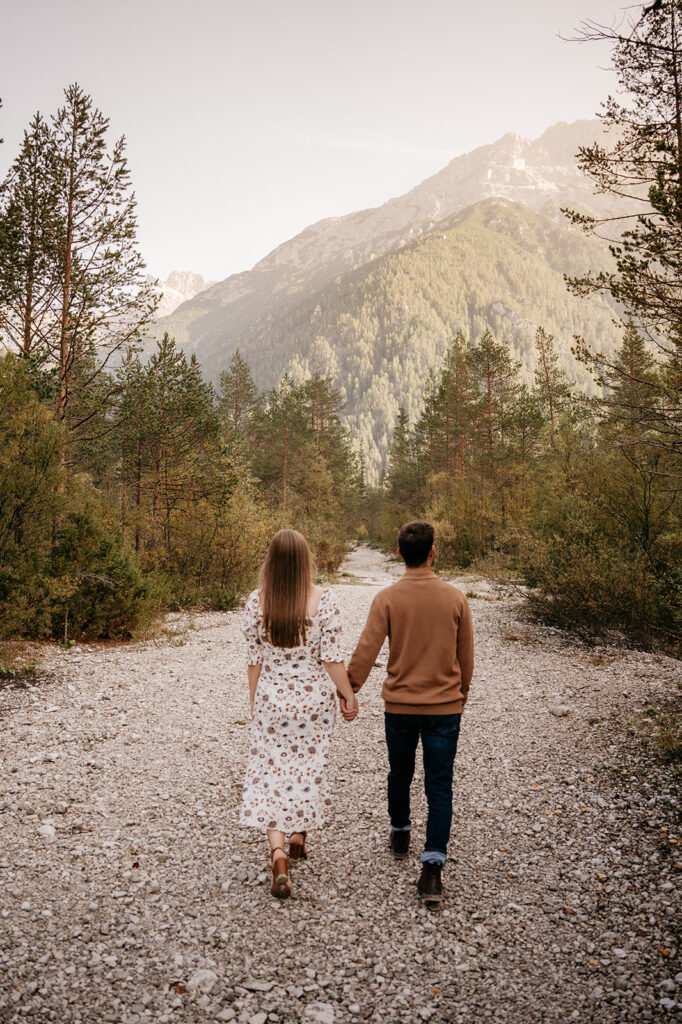 Couple walking on mountain path surrounded by trees.