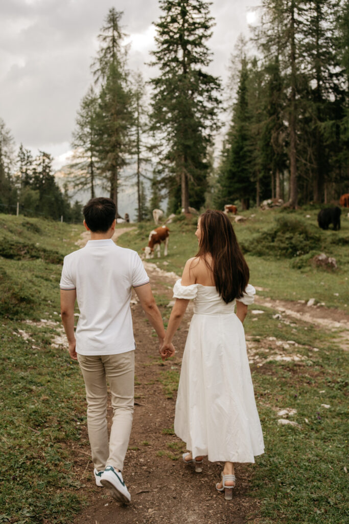 Couple walking hand in hand through forest path.