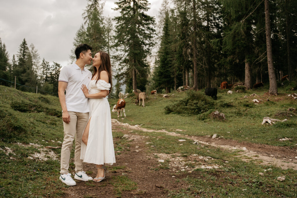 Couple embracing in scenic forest with cows nearby.