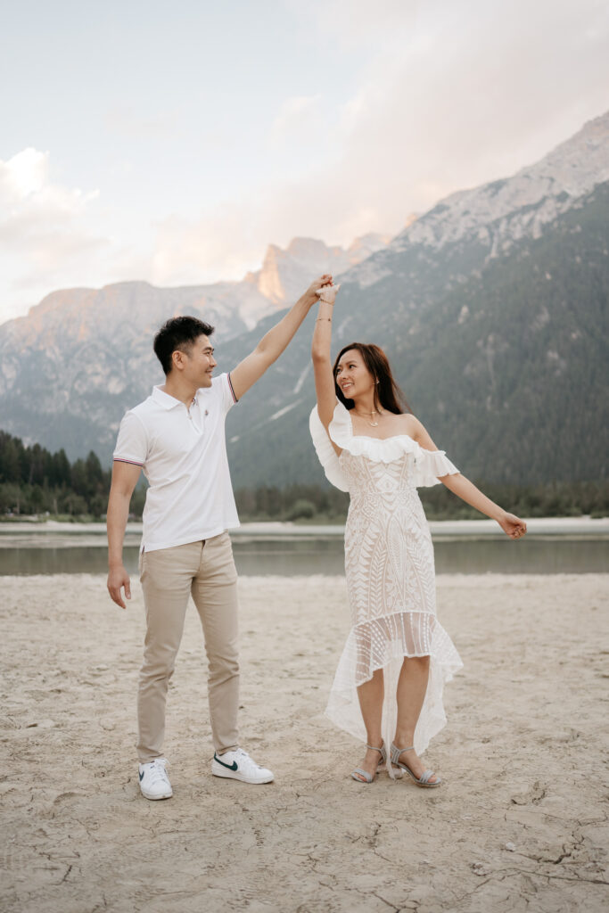 Couple dancing on beach with mountains backdrop.