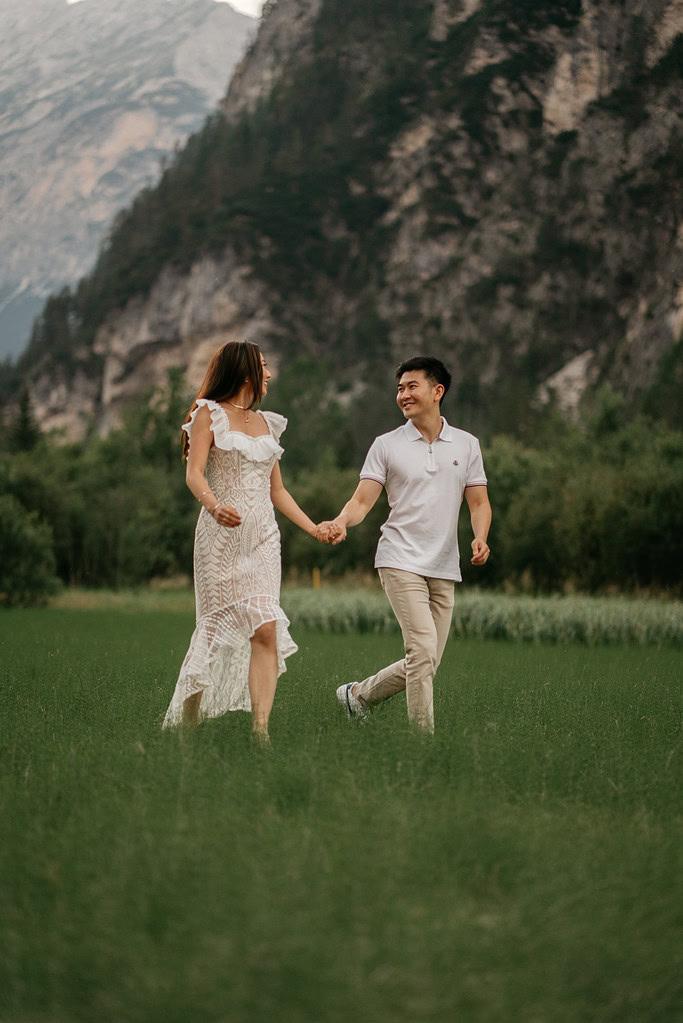 Couple walking hand-in-hand in green field.