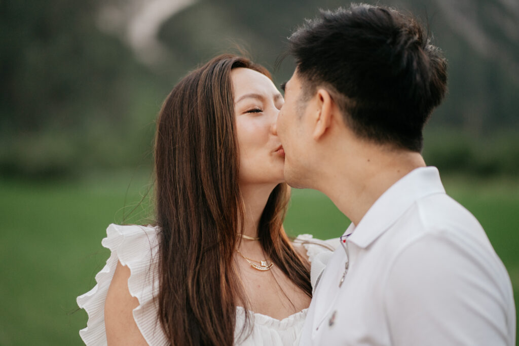 Couple kissing outdoors in a green field.