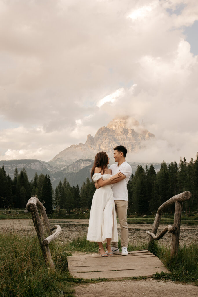 Couple embracing on bridge with mountain background.