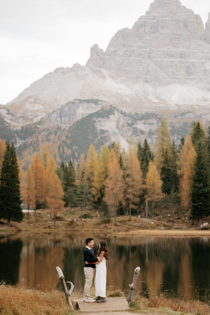 Couple standing on dock by a lake, mountain background.