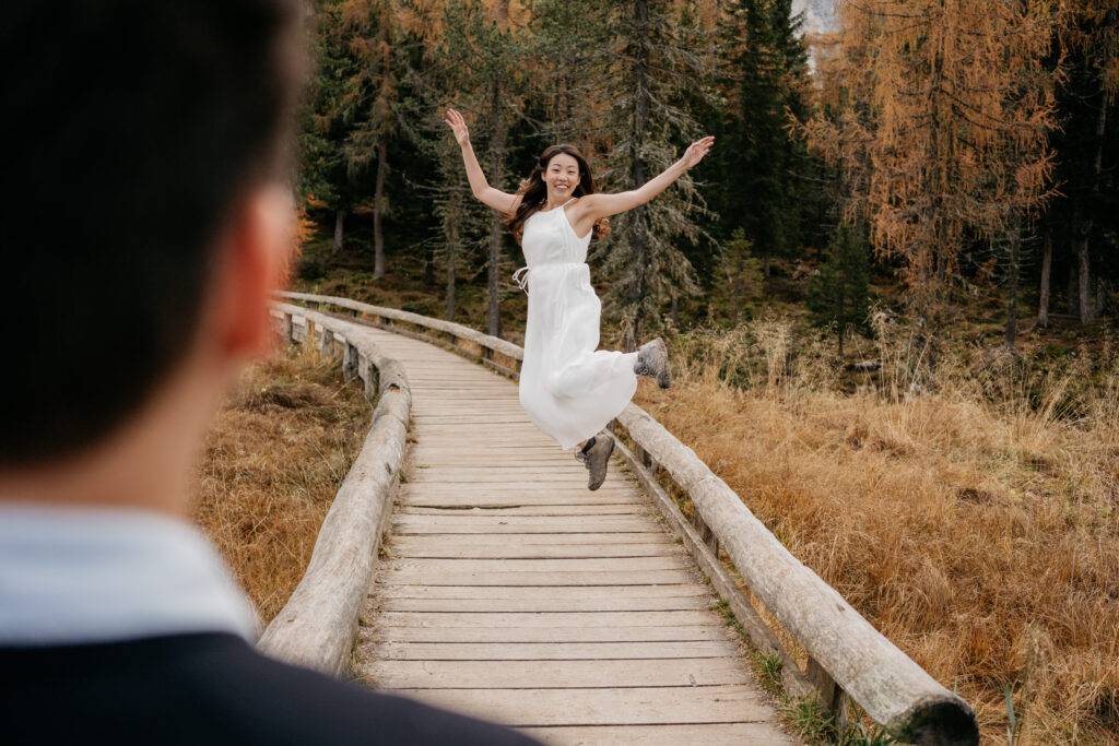 Woman in white dress joyfully jumping on bridge.