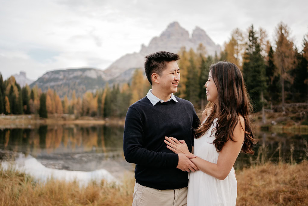 Couple smiling by serene lake and mountains.