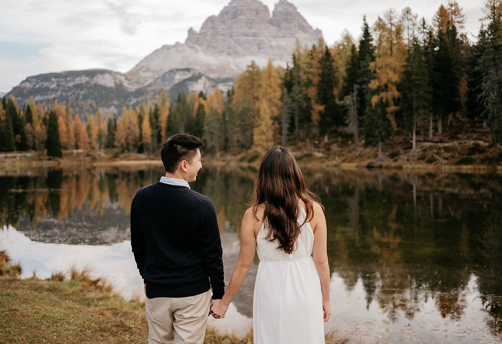 Couple holding hands by a serene mountain lake.