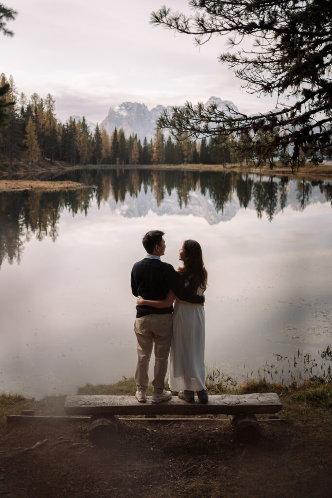 Couple embracing by peaceful mountain lake at sunset.