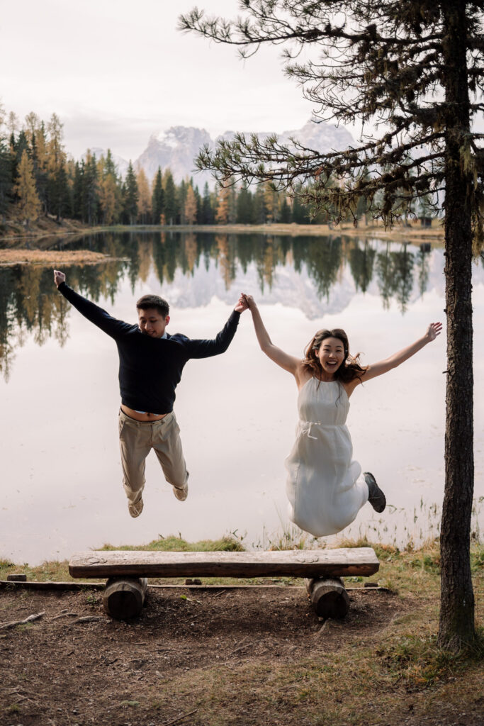 Couple joyfully jumping by lake with scenic view.