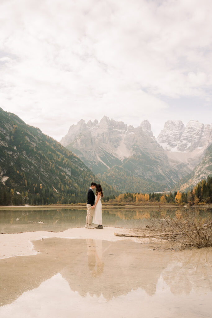 Couple embraces by mountain lake with reflections.