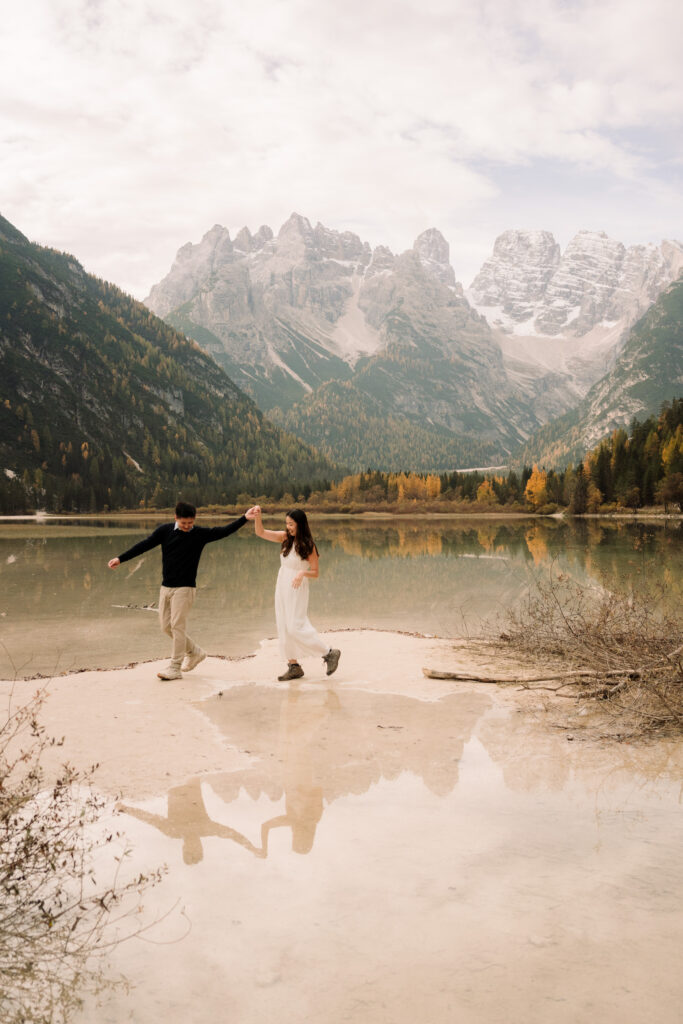 Couple walking by lake with mountain backdrop.