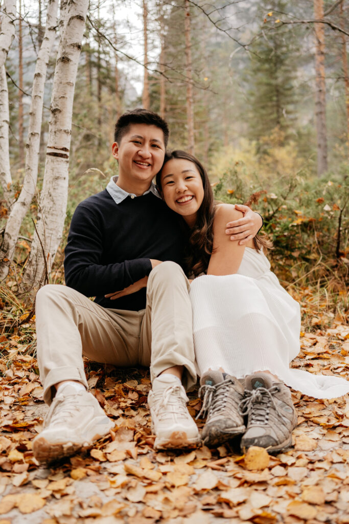 Couple sitting in autumn forest, smiling.