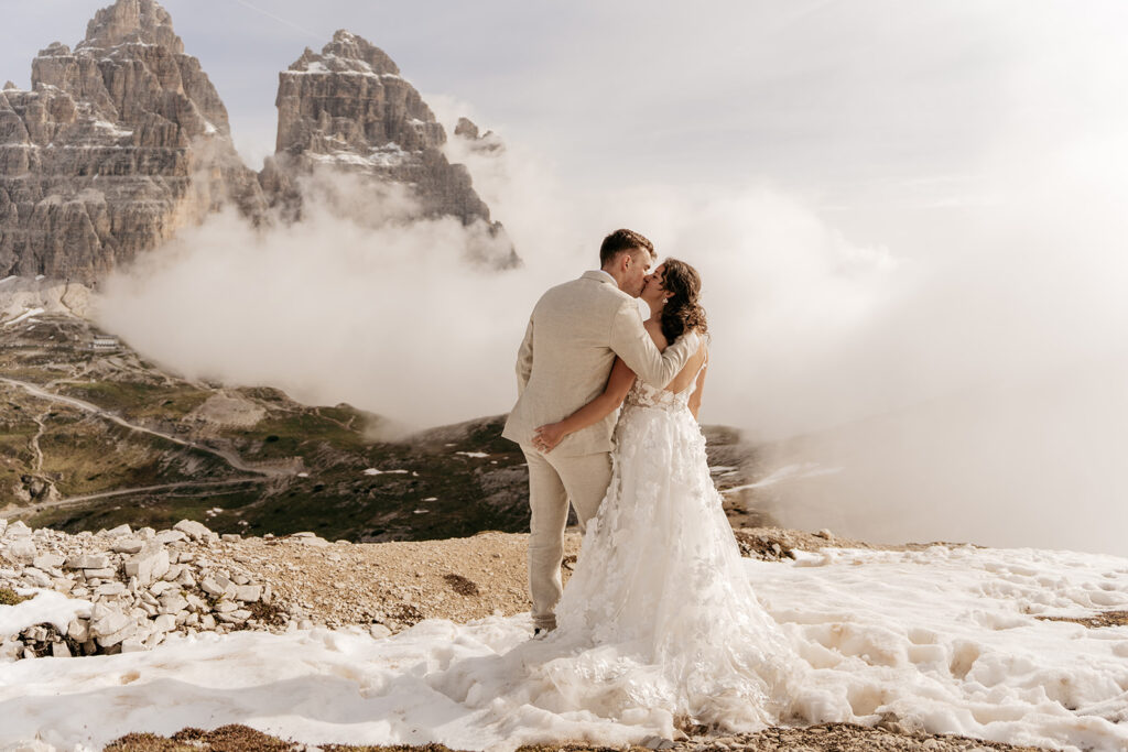 Bride and groom kiss on snowy mountain summit.