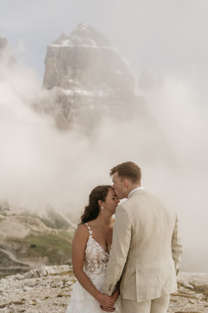 Bride and groom kiss in misty mountain landscape.