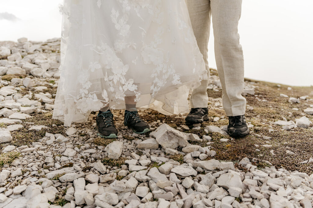 Bride and groom in hiking shoes on rocky terrain.