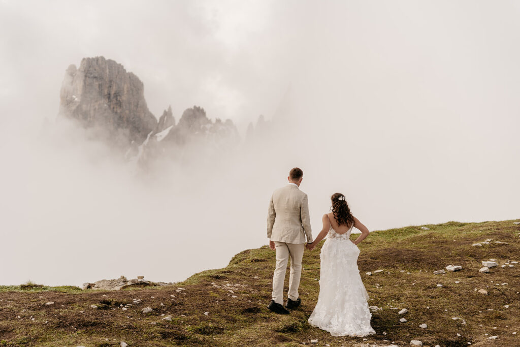 Couple holding hands on foggy mountain path.