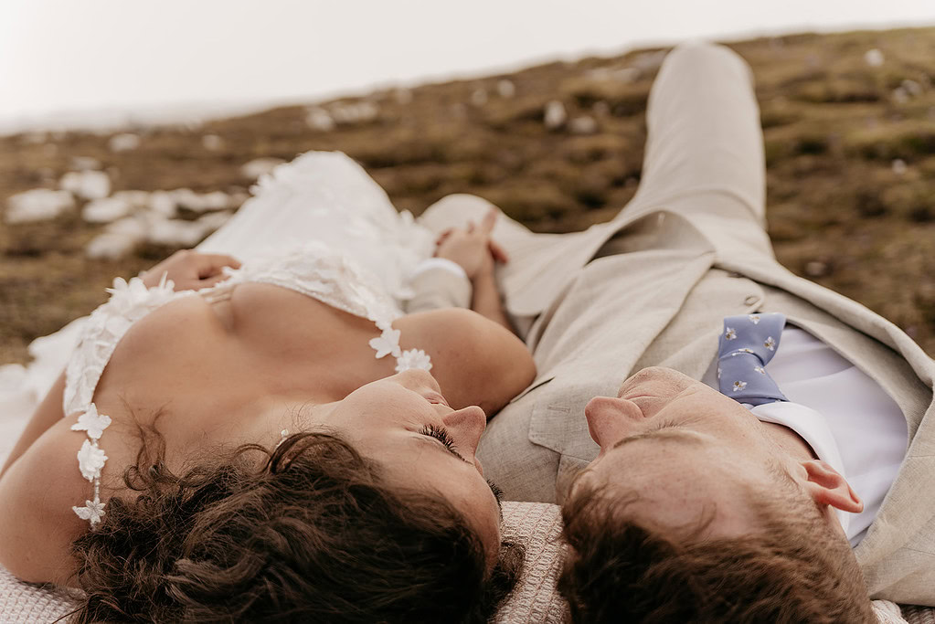 Bride and groom lying on grass, holding hands.